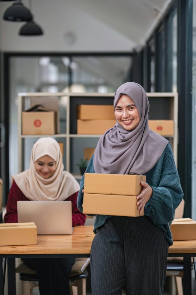 A happy young Asian Muslim female online seller working with her employee in the office. SME