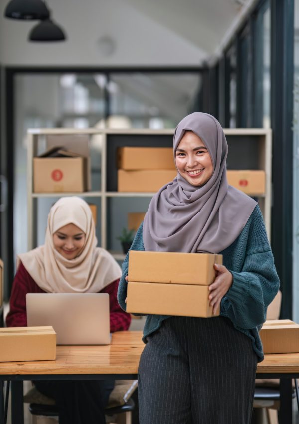 A happy young Asian Muslim female online seller working with her employee in the office. SME
