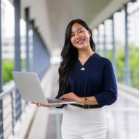 Portrait of smiling businesswoman working on laptop in office corridor
