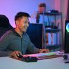 Smiling Asian male gamer playing video game at gaming room at night.